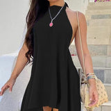 Woman wearing a black halter neck mini dress with a loose, flowy fit, accessorized with a nude shoulder bag and bracelets in an outdoor setting.

